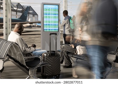 Checking electronic flights timetable, fast movement and multiethnic passengers sitting on airport benches, reading FIDS display schedule, high volume airport traffic and diverse group of people.
