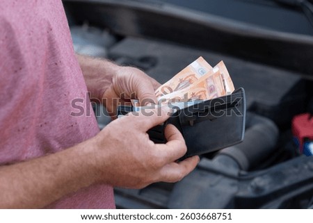 Checking euro cash while fixing a car at the roadside on afternoon. A person examines euro cash in their wallet, standing by an open car hood, counting repair cost
