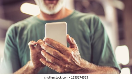 Checking The Exercise Plan. Senior Man At Gym Using Smart Phone. Close Up. Focus Is On Hands.