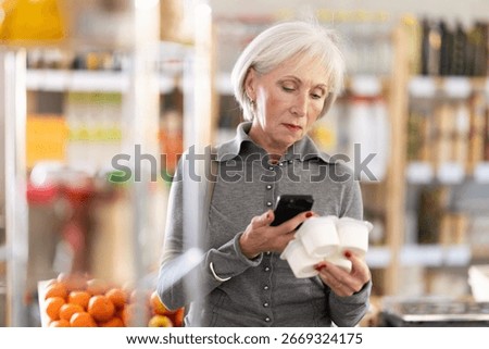 Checking expiration date of yogurt - elderly female shopper scans QR code on label of yogurt using her smartphone