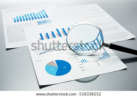 Checking financial reports. Graphs and charts. Documents and magnifying glass on gray reflection background.
