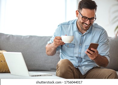 Checking his messages over coffee. Cropped shot of a handsome young man checking his messages while drinking coffee at home. Man using a smart phone while drinking coffee at home - Powered by Shutterstock