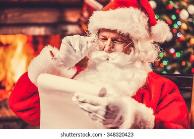 Checking his special list. Traditional Santa Claus sitting at his chair and reading a letter with fireplace and Christmas Tree in the background - Powered by Shutterstock