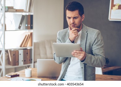 Checking his timetable. Handsome young man working with touchpad and looking confused while standing in office - Shutterstock ID 403543654