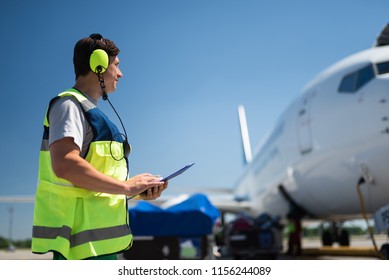 Checking the jet. Side view of airport crew member. Man wearing headphones and holding the clipboard - Powered by Shutterstock