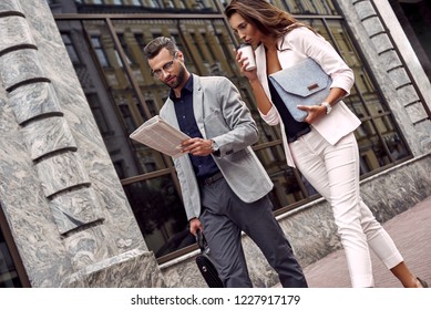 Checking Latest News. Two Young Business People Walking Outside On The City Street Man Reading Newspaper While Woman Drinking Hot Coffee