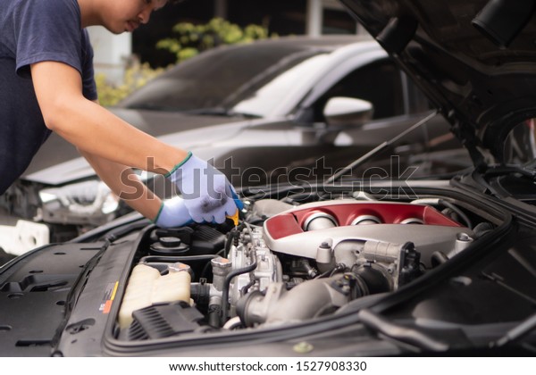 Checking the\
motor oil for the trip ,The car mechanic staff is pulling the oil\
level gauge up to check the oil\
level.
