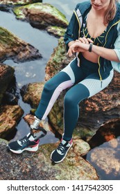 Checking Results. Cropped Photo Of Disabled Athlete Woman In Sportswear With Prosthetic Leg Checking Pedometer While Sitting On The Stone