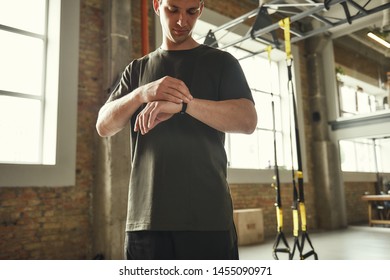 Checking Results. Young Man In Sports Clothing Checking Pedometer While Standing At Gym