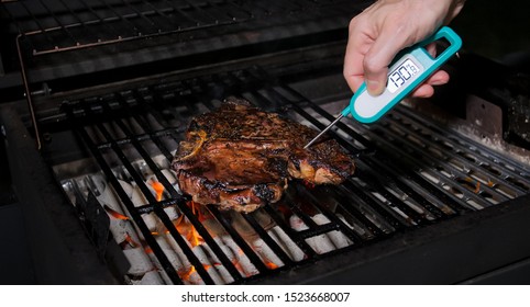 Checking for safe food temperature with digital instant thermometer. Cook measuring temperature of freshly grilled steak on hot barbecue grill.