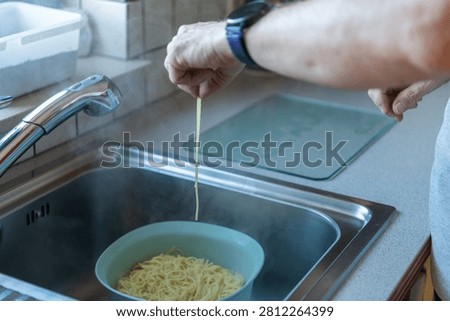 Checking spaghetti doneness by lifting a single pasta strand above a colander after draining