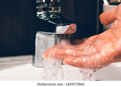 checking the temperature by touching the running water with your hand. Close-up on fingers under hot water from the tap sink or bath in the bathroom at home