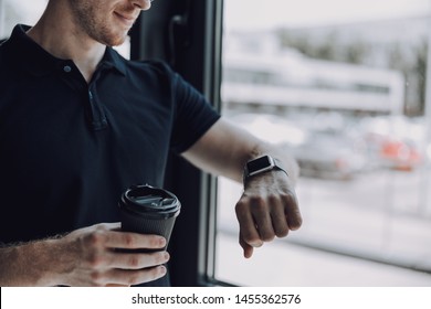 Checking the time. Close up of a man in black polo shirt putting hand up and looking at smart watch while holding a carton cup of coffee - Powered by Shutterstock