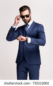 Checking The Time. Handsome Young Man In Sunglasses Looking At His Watch While Standing Against White Background.