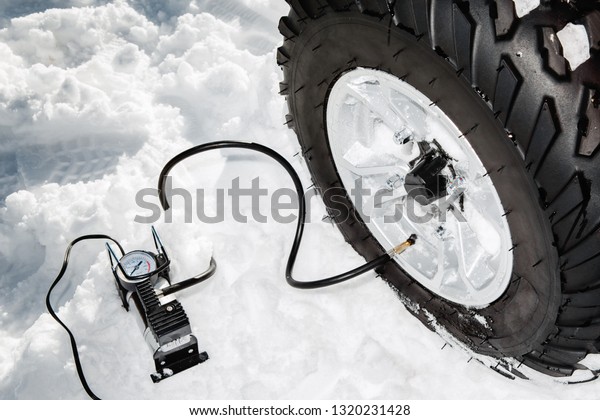 Checking tire pressure. Pumping air\
into auto wheel on the ATV 4wd quad bike stand in heavy\
snow.