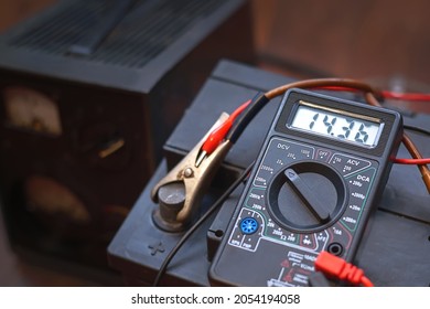 Checking voltage with multimeter and charging car battery with charger from home electricity. Recovery of acid batteries, resuscitate car battery. Voltmeter to check voltage level on car battery - Shutterstock ID 2054194058