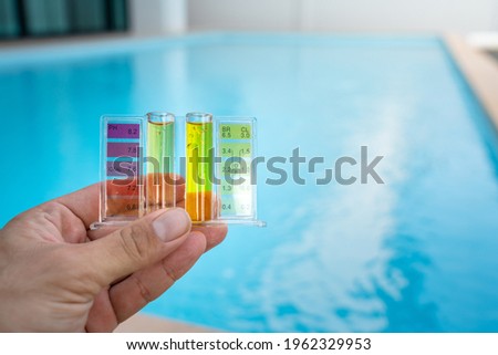 Checking water quality of swimming pool by using chemical test kit to compare PH and chlorine concentration, photo with blurred background of clearly blue water surface.