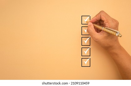 Checklist concept. White marking on checklist box isolated on an orange background. Hand holding a pen and checklist with copy space. Close-up photo. Top view.