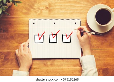 Checklist With A Person Holding A Pen On A Wooden Desk