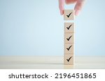 Checklist, Task list, Survey and assessment. Quality Control. Goals achievement and business success. Hand holding Check mark on wooden blocks for complete check list.