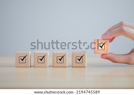 Checklist, Task list, Survey and assessment. Quality Control. Goals achievement and business success. Hand holding Check mark on wooden blocks for complete check list.