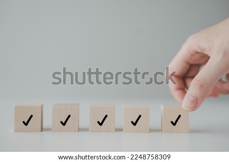 Checklist, Task list, Survey and assessment. Quality Control. Goals achievement and business success. Hand holding Check mark on wooden blocks for complete check list.