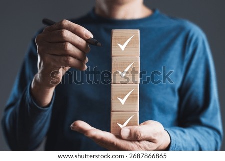Checklist and task management concept with hand holding stacked wooden blocks marked with check symbols for completed goals, planning, organization, and productivity.