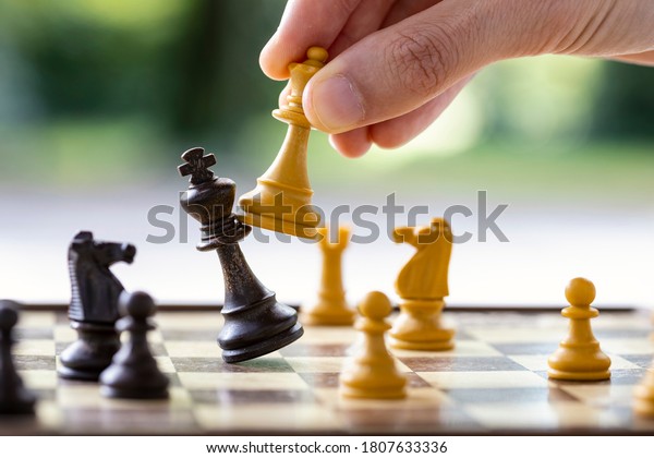 Checkmate. A man\'s hand is\
hitting the king with the queen in a chess game. Concept for\
playing chess outdoor, end of the game, end of the match, business\
strategy. 