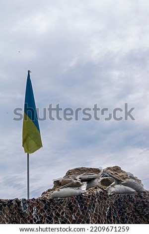 checkpoint with the flag of Ukraine of camouflage military mesh and sandbags on a cloudy day. war in Ukraine, vertical