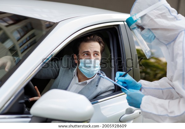 Checks passengers and driver for virus, man in\
biological suit writes data on tablet, COVID-19 quarantine,\
medicine, health care. Male in protective mask waiting coronavirus\
test in car, close up