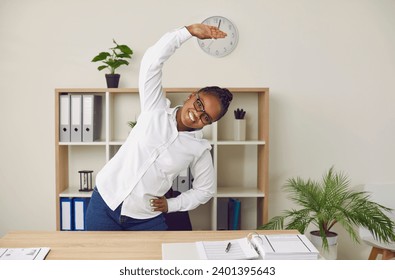 Cheeful business woman doing stretching exercise behind table at workplace. African American woman doing side bending posture fitness exercises during break. Healthy lifestyle concept