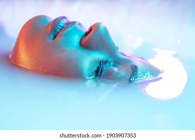 Cheeks. Beautiful female face in the milk bath with soft glowing in blue-pink neon light. Copyspace for advertising. Modern neoned colors, foam. Beauty, fashion, style, skincare concept. Attractive.