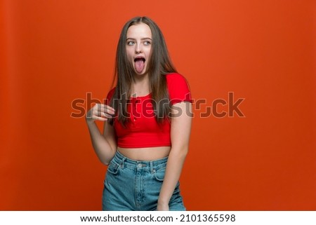 Cheeky modern young cool girl showing tongue posing looking aside on orange background with copy space for advertisement