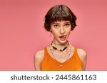 cheeky playful girl in 20s with short brunette hair sticking tongue out on pink background