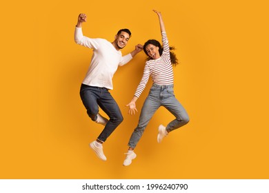 Cheerful Active Arab Couple Jumping In Air Over Yellow Background, Joyful Emotional Middle Eastern Man And Woman Having Fun Together, Raising Hands And Exclaiming With Excitement, Full Length - Shutterstock ID 1996240790