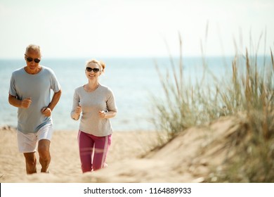 Cheerful and active couple of retired spouses jogging in the morning on the beach