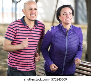 Cheerful Active Mature Couple Jogging Together At Park
