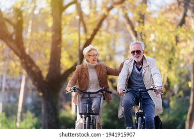 Cheerful active senior couple with bicycle in public park together having fun. Perfect activities for elderly people. Happy mature couple riding bicycles in park - Powered by Shutterstock