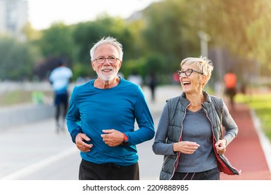 Cheerful active senior couple jogging together outdoors along the river. Healthy activities for elderly people.