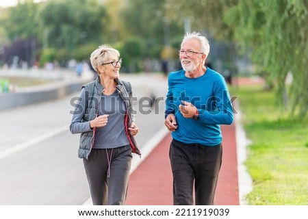 Cheerful active senior couple jogging together outdoors along the river. Healthy activities for elderly people. BeH3althy