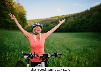 Cheerful active senior woman biker raising arms outdoors in nature. - Shutterstock ID 2119431071