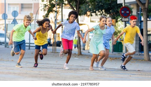 Cheerful Active Tween Boys And Girls In Colorful Clothes Running Holding Hands Along Summer City Street.