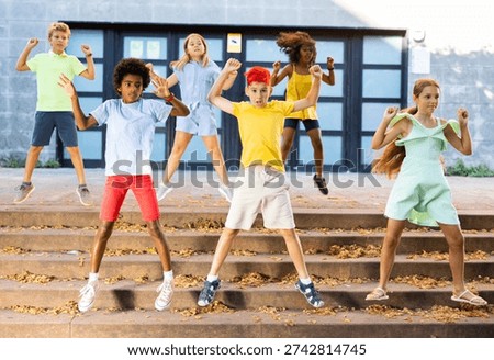 Cheerful active tweenagers synchronously jumping up while dancing together on steps on summer city street..