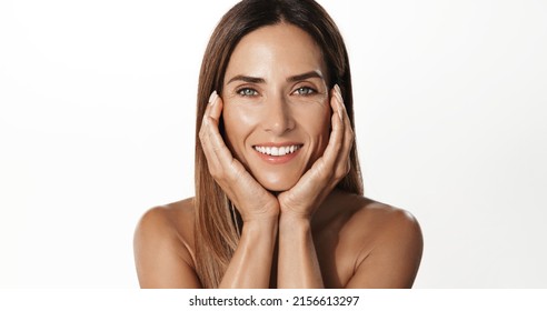 Cheerful Adult, 50 Years Woman With Hands On Her Face Against White Background. Happy Mature Woman With Bare Shoulders, Glowing Skin Without Wrinkles