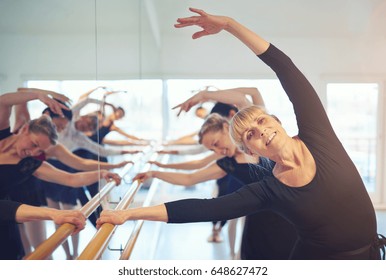 Cheerful adult female ballet dancer looking at camera and stretching with hand up.