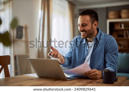 A cheerful adult hiring manager laughing with a candidate in an online interview making a positive atmosphere while holding his resume papers and application.