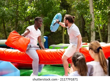 Cheerful Adult Men Having Fun On Inflatable Pillow Fight Arena In Outdoor Amusement Park