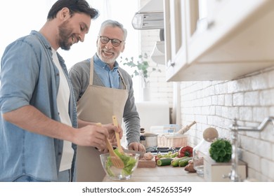 Cheerful adult son helping his senior old father in cooking, preparing family meal, dinner, lunch. Parents visiting. Happy father`s day! I love you, dad! Men cooking together - Powered by Shutterstock