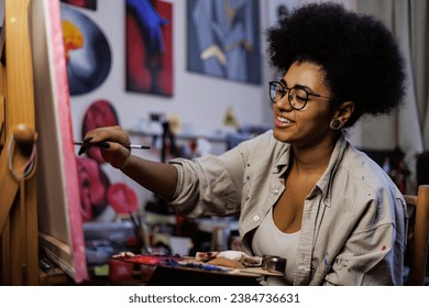 Cheerful african american artist painting on canvas in art workshop	 - Powered by Shutterstock