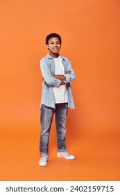 cheerful african american boy posing joyfully with arms crossed on chest on orange backdrop